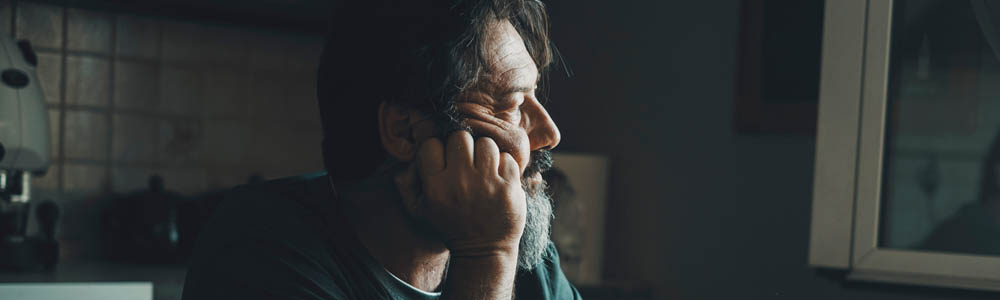 Depressed man sitting at his kitchen table, looking out the window